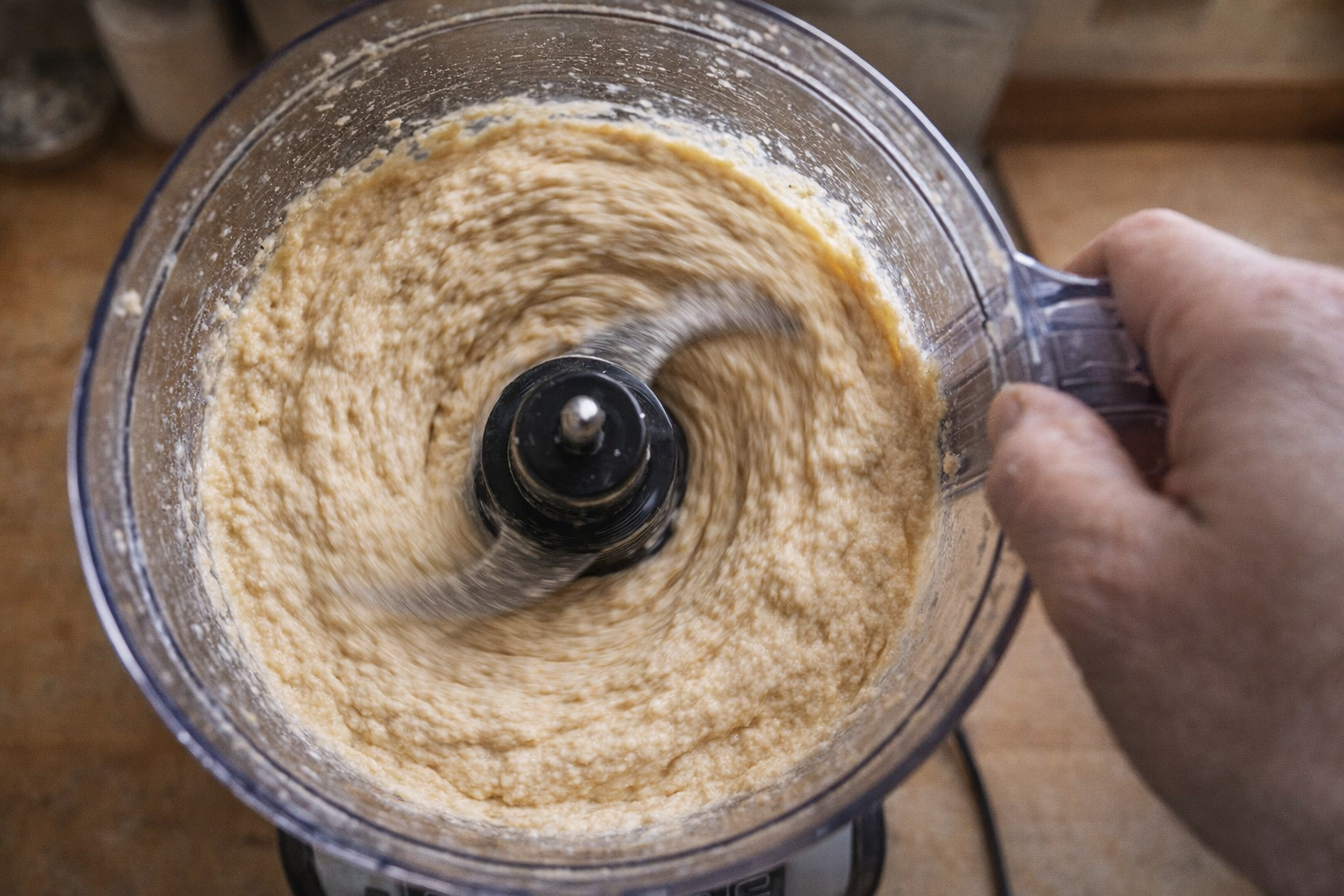 An overhead shot of hummus being blended in a food processor, showing the creamy texture and the blades in motion